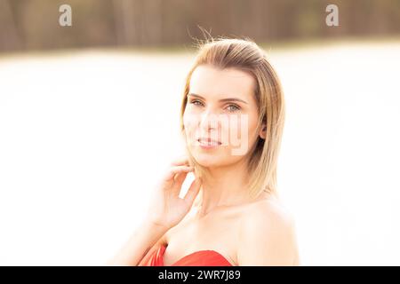 Doucement illuminée par le soleil de l’heure dorée, une jeune femme pose gracieusement, son regard serein et son sourire subtil évoquant un sentiment de confiance paisible. Beauté sereine : jeune femme dans le portrait trempé de soleil. Photo de haute qualité Banque D'Images