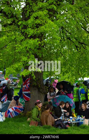 Les gens s'abritent de la pluie sous un arbre alors qu'ils se rassemblent pour voir le couronnement du roi Charles III à l'écran à Hyde Park, Londres. Banque D'Images