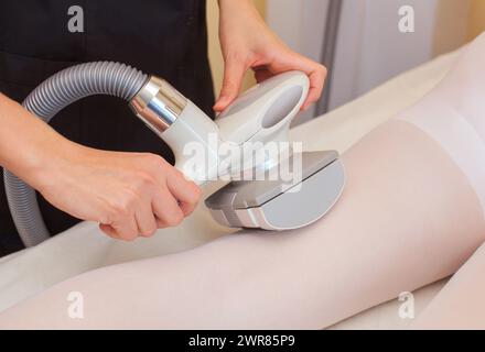 Le masseur fait un massage matériel sur les jambes du patient dans un costume blanc, gros plan dans un salon de beauté. Banque D'Images