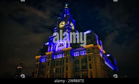 Le légendaire Royal Liver Building de Liverpool la nuit, illuminé de lumières bleues et jaunes sur un ciel sombre. Banque D'Images