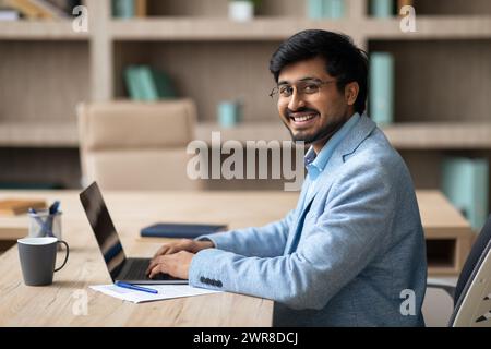 Homme d'affaires indien utilisant un ordinateur portable est assis au bureau souriant à la caméra Banque D'Images