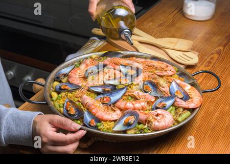 Verser de l'huile d'olive dans une paella aux fruits de mer, rehausser les saveurs de ce plat espagnol classique, cuisine espagnole typique, Majorque, Îles Baléares, Espagne Banque D'Images