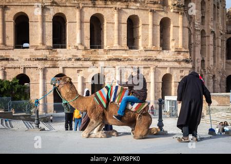 Deux jeunes garçons font une promenade à dos de chameau à l'extérieur de l'amphithéâtre romain El Jem (Thysdrus), bien conservé, en Tunisie. Banque D'Images