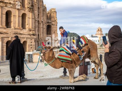 Deux jeunes garçons font une promenade à dos de chameau à l'extérieur de l'amphithéâtre romain El Jem (Thysdrus), bien conservé, en Tunisie. Banque D'Images