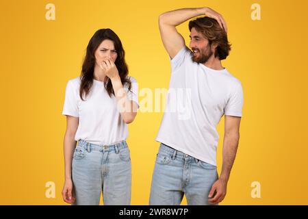 Une femme se pince le nez avec une expression dégoûtée tandis qu'un homme se gratte la tête avec un sourire Banque D'Images