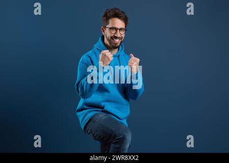 Joyeux homme barbu en sweat à capuche bleu levant les poings en triomphe Banque D'Images