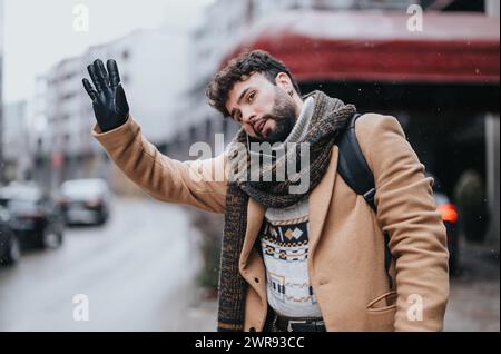 Jeune homme d'affaires confiant saluant un taxi dans un environnement urbain enneigé. Banque D'Images