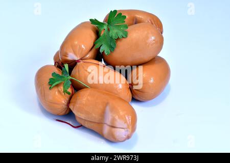 Des saucisses de viande de porc et quelques feuilles vertes reposent sur un fond blanc. Banque D'Images