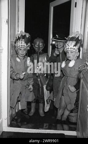 années 1960, historique, jeunes garçons en costumes.. Deux comme des indiens rouges avec de la peinture pour le visage, un cow-boy et un centurion romain, debout ensemble sur une porte, Angleterre, Royaume-Uni. Banque D'Images