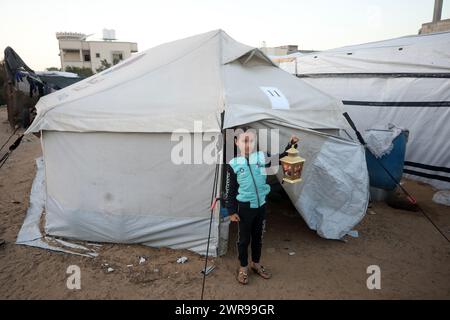 Rafah, Gaza. 11 mars 2024. Une jeune fille palestinienne déplacée porte des lanternes traditionnelles « fanous » au milieu de tentations de fortune pendant les célébrations pour le début du mois de jeûne sacré musulman du Ramadan à Rafah, en Ontario, dans le sud de la bande de Gaza, le lundi 11 mars 2024. Photo de Ismael Mohamad/UPI. Crédit : UPI/Alamy Live News Banque D'Images