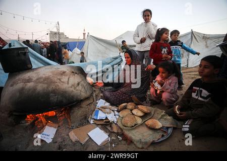 Rafah, Gaza. 11 mars 2024. Déplacée, une palestinienne cuit du pain sur un vieux four en argile, au milieu de tentes de fortune dans le camp de réfugiés de Rafah, le premier jour du mois sacré du Ramadan musulman à Rafah, Gaza, lundi 11 mars 2024. Crédit : UPI/Alamy Live News Banque D'Images