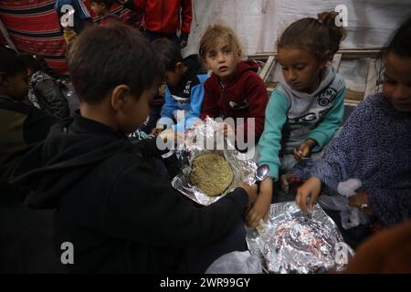 Rafah, Gaza. 11 mars 2024. Les Palestiniens déplacés ont un dîner de rupture rapide (iftar) au milieu de tentes de fortune dans le camp de réfugiés de Rafah, le premier jour du Ramadan du mois sacré des musulmans à Rafah, Gaza, le 11 mars 2024. Photo de Ismael Mohamad/UPI crédit : UPI/Alamy Live News Banque D'Images