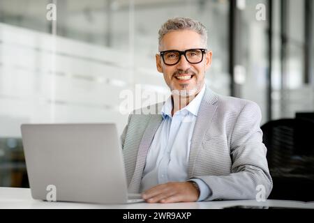 Homme d'affaires confiant est capturé avec un large sourire engageant alors qu'il travaille dans un espace d'entreprise aéré et bien conçu, mettant l'accent sur l'accessibilité et le professionnalisme Banque D'Images
