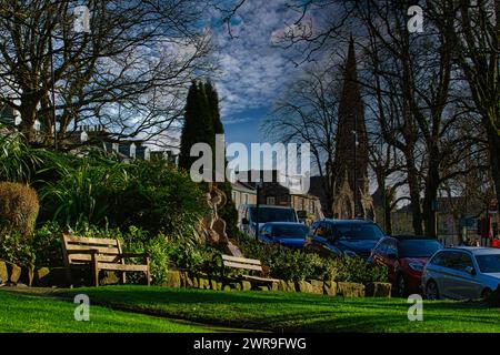 Scène de parc urbain tranquille avec des bancs et une végétation luxuriante, sur fond de bâtiments historiques et ciel bleu avec des nuages tortueux à Harrogate, en Banque D'Images