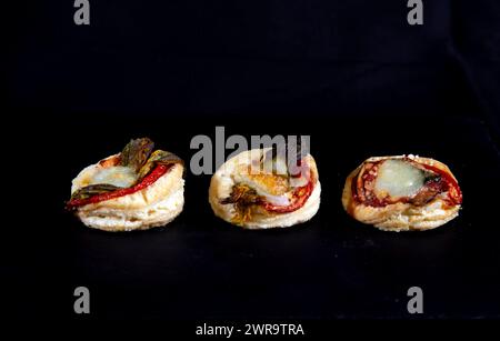 Trois petites pâtisseries salées rustiques, avec pâte feuilletée, tomates, mozzarella et fleurs de courgette, sur fond noir Banque D'Images