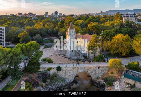 Proche aérien de coucher de soleil coloré sur le Musée de Conde de Castro Guimaraes, Cascais, Portugal. Bel immeuble dans un endroit pittoresque, à côté de la piscine de marée, plage de sable, rivages rocheux et pont, stylisé comme château Manueline. Banque D'Images