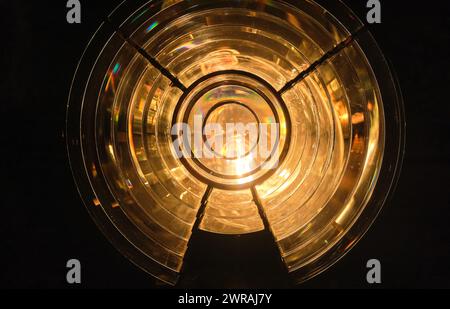 Image rapprochée du prisme de verre constituant la lentille de Fresnel avec lumières allumées. Utilisé dans les phares et les lanternes de phare pour concentrer la lumière de la lampe compacte dans des faisceaux lumineux rotatifs ou des flashs. Forme ronde, pièce sombre, lumières allumées. Banque D'Images