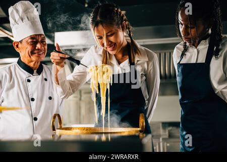 Chef éduque en cuisine. Les écolières font des nouilles japonaises. Enfants et professeur à poêle. Souriant Banque D'Images