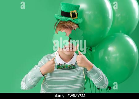 Mignon petit garçon avec chapeau de leprechaun, trèfles et ballons sur fond vert. Prog Célébration de la fête de Patrick Banque D'Images