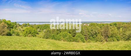 Vue panoramique depuis une colline sur une forêt verdoyante à feuilles caduques avec un lac à l'horizon lors d'une belle journée d'été ensoleillée Banque D'Images