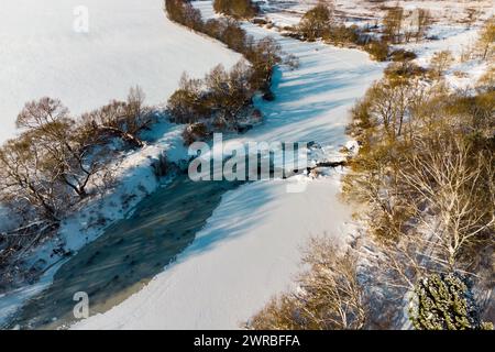 Vue depuis un drone d'une rivière couverte de glace et de neige où se jette un petit ruisseau Banque D'Images