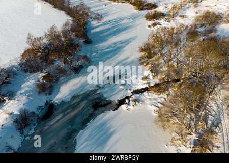 Vue depuis un drone d'une rivière couverte de glace et de neige où se jette un petit ruisseau Banque D'Images