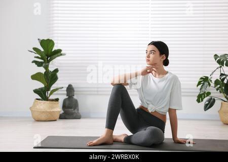 Belle fille assise sur le tapis de yoga en studio Banque D'Images