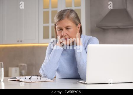 Ménopause. Femme souffrant de douleur dans le cou à table dans la cuisine, espace pour le texte Banque D'Images