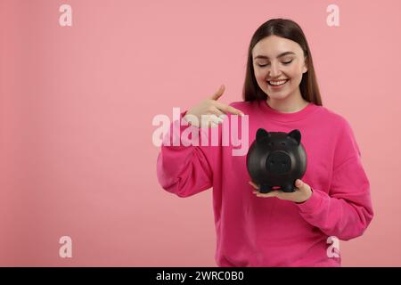 Femme heureuse pointant à la tirelire sur fond rose, espace pour le texte Banque D'Images