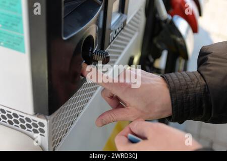 La main d'une femme pousse une carte bancaire dans un guichet automatique d'une station-service Banque D'Images