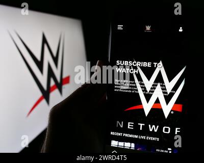 Personne tenant le téléphone portable avec la page Web de la société de promotion World Wrestling Entertainment (WWE) devant le logo. Concentrez-vous sur le centre de l'écran du téléphone. Banque D'Images