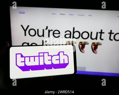Personne tenant un smartphone avec le logo de la société américaine de streaming en direct Twitch Interactive Inc en face du site Web. Concentrez-vous sur l'affichage du téléphone. Banque D'Images