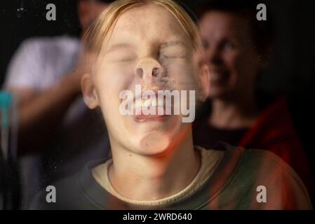 Portrait d'une adolescente à travers son visage appuyé contre le verre sur un fond sombre. Des pitreries drôles Banque D'Images