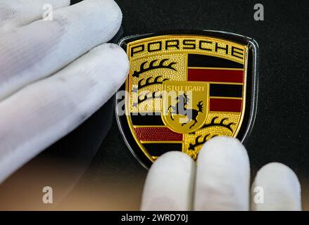 Leipzig, Allemagne. 11 mars 2024. Un employé appose le logo de la marque sur une Porsche de l'usine de Leipzig. Le constructeur de véhicules sportifs et tout-terrain Porsche publiera ses chiffres d'affaires de l'année écoulée mardi 12 mars à l'usine Porsche de Leipzig. Crédit : Jan Woitas/dpa/Alamy Live News Banque D'Images