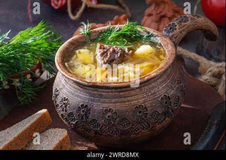 soupe de chou dans un pot en argile. Soupe russe traditionnelle de choucroute et de chou blanc, viande et pommes de terre dans un pot en argile, fond en bois vintage, rouille Banque D'Images