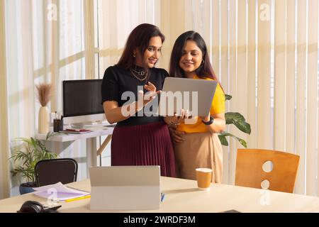 Deux femmes d'affaires discutant projet sur ordinateur portable au poste de travail de bureau Banque D'Images