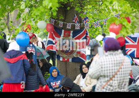 Les gens s'abritent de la pluie sous un arbre alors qu'ils se rassemblent pour voir le couronnement du roi Charles III à l'écran à Hyde Park, Londres. Banque D'Images