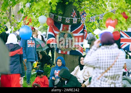 Les gens s'abritent de la pluie sous un arbre alors qu'ils se rassemblent pour voir le couronnement du roi Charles III à l'écran à Hyde Park, Londres. Banque D'Images