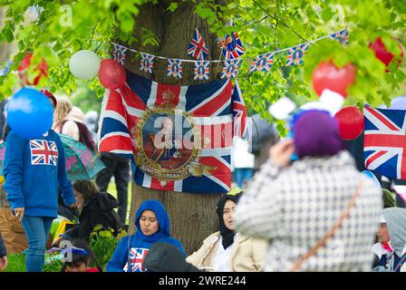 Les gens s'abritent de la pluie sous un arbre alors qu'ils se rassemblent pour voir le couronnement du roi Charles III à l'écran à Hyde Park, Londres. Banque D'Images