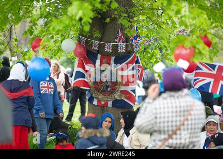 Les gens s'abritent de la pluie sous un arbre alors qu'ils se rassemblent pour voir le couronnement du roi Charles III à l'écran à Hyde Park, Londres. Banque D'Images