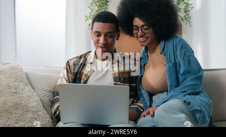 Couple de famille heureux femme de mari afro-américain sur canapé homme femme à canapé ordinateur portable achats en ligne d'achat dans la réservation de magasin d'application Internet Banque D'Images