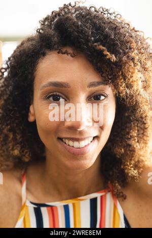 Femme biraciale aux cheveux bouclés sourit chaleureusement, ses yeux brillants de joie Banque D'Images