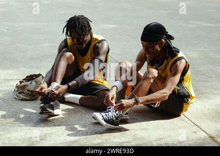 Hommes noirs joyeux attachant des lacets de chaussures avant le match de streetball Banque D'Images