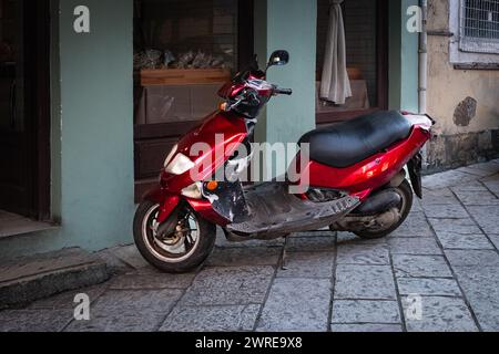 Scooter rouge garé sur un trottoir dans la vieille ville. Scooter un des transports les plus populaires en Europe. Scène de rue typique en Grèce avec un scooter outsi Banque D'Images