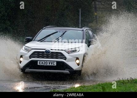 Une voiture traverse une route inondée sous de fortes pluies près de Folkestone dans le Kent. Date de la photo : mardi 12 mars 2024. Banque D'Images