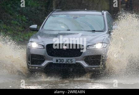 Une voiture traverse une route inondée sous de fortes pluies près de Folkestone dans le Kent. Date de la photo : mardi 12 mars 2024. Banque D'Images