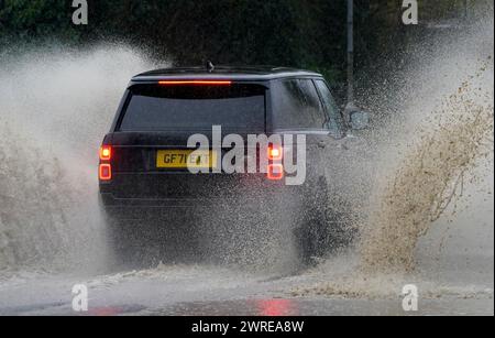 Une voiture traverse une route inondée sous de fortes pluies près de Folkestone dans le Kent. Date de la photo : mardi 12 mars 2024. Banque D'Images