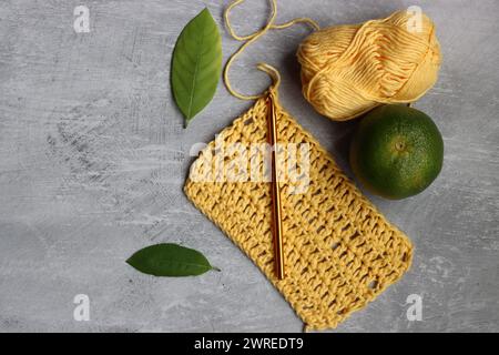 Crochet écharpe en cours. Crochet crochet, fil de coton jaune, citron vert et feuilles sur fond gris, vue de dessus Banque D'Images