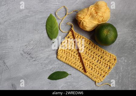 Crochet écharpe en cours. Crochet crochet, fil de coton jaune, citron vert et feuilles sur fond gris, vue de dessus Banque D'Images