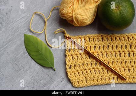 Crochet écharpe en cours. Crochet crochet, fil de coton jaune, citron vert et feuilles sur fond gris, vue de dessus Banque D'Images